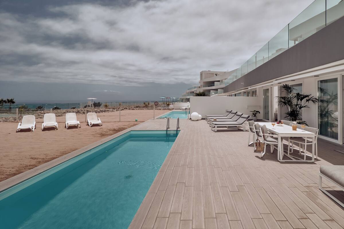 A poolside area with sun loungers, a dining table with chairs, and a large TV.