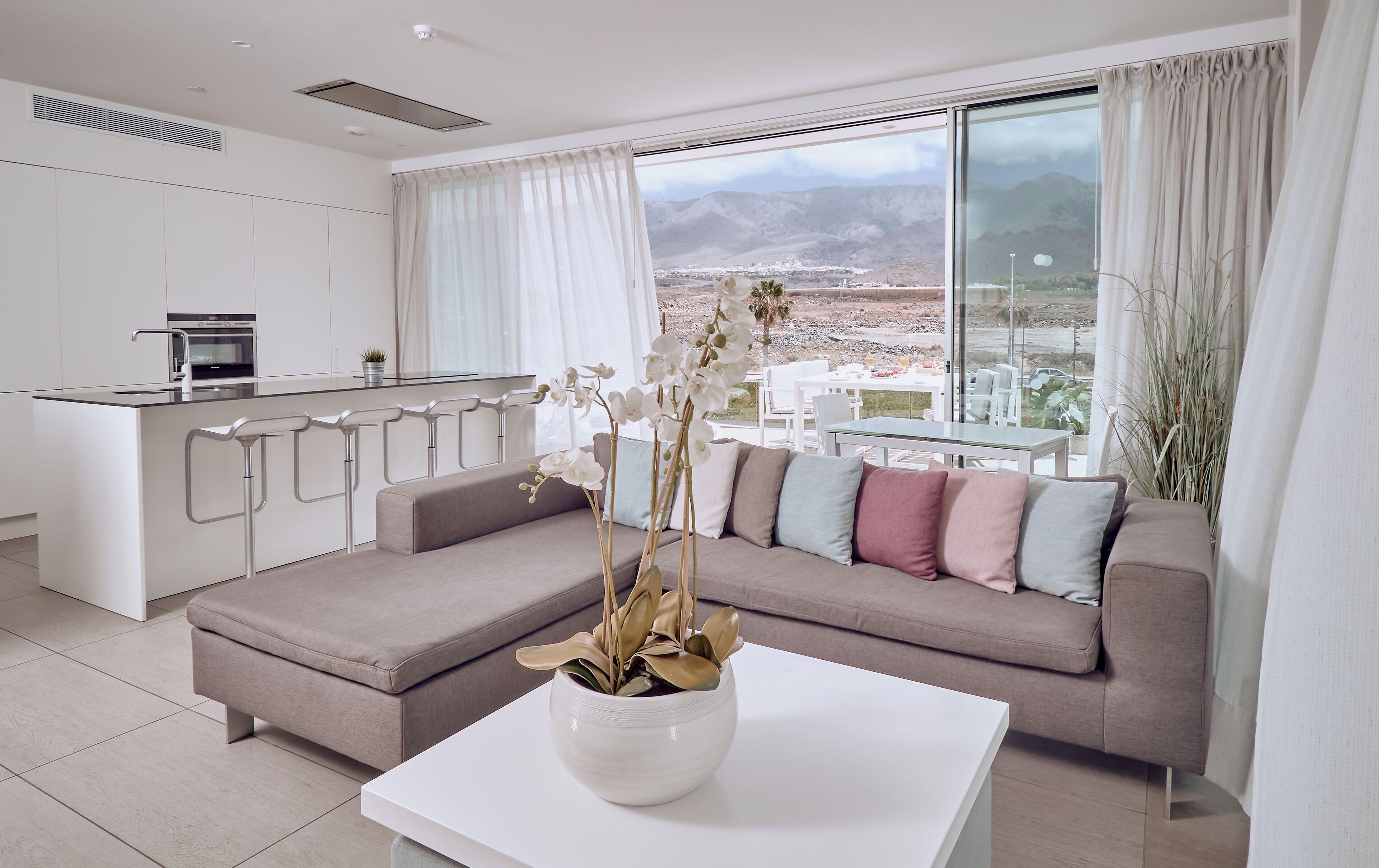A modern living room with a sofa, a coffee table, and a view of a cityscape through large windows.
