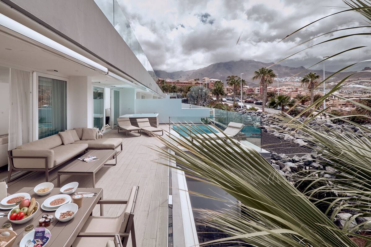 A modern outdoor dining area with a pool and mountain views.