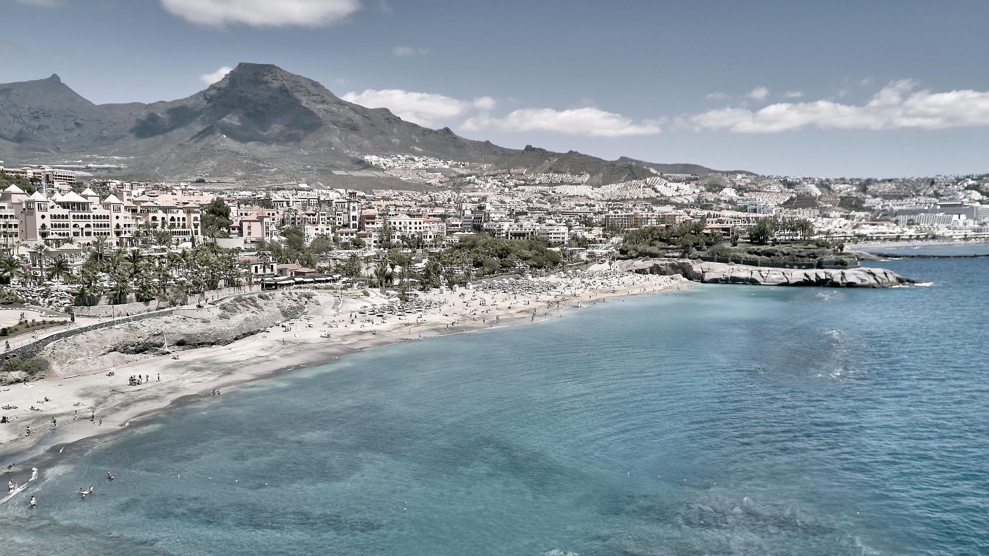 A coastal cityscape with a beach, buildings, and a mountain in the background.