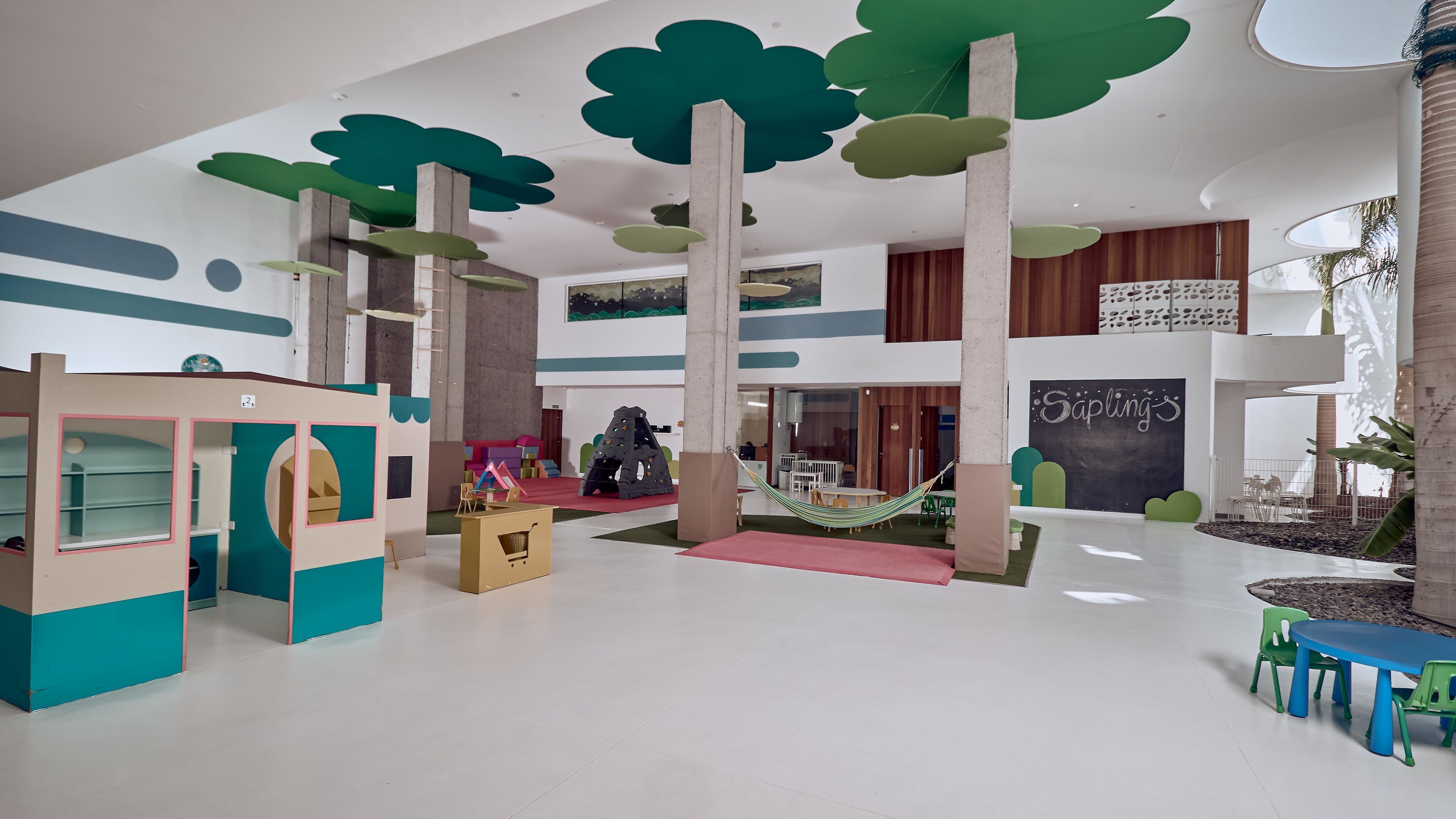 A spacious indoor area with a play area, a seating area with a table and chairs, and a large chalkboard with writing.