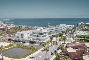 Un hotel moderno con fachada curva, estacionamiento y palmeras.
