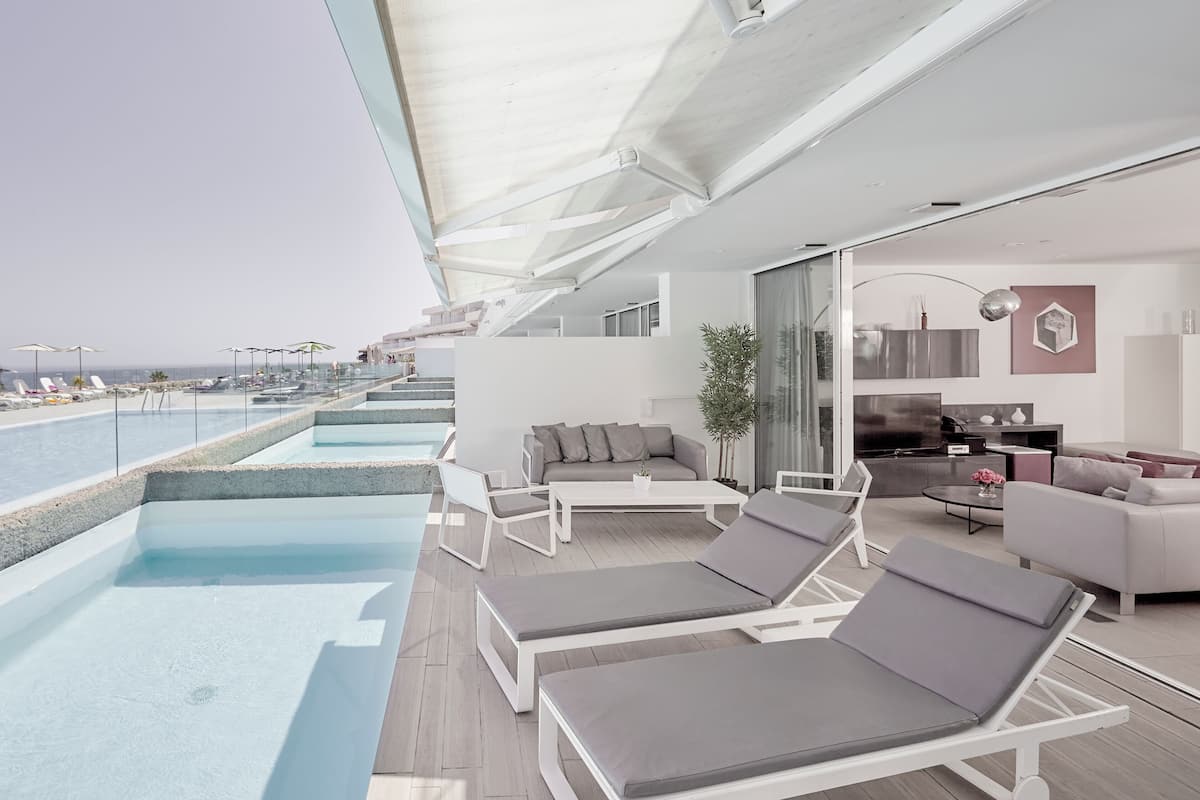 A modern outdoor balcony with a pool, lounge chairs, and a seating area with a sofa and coffee table.