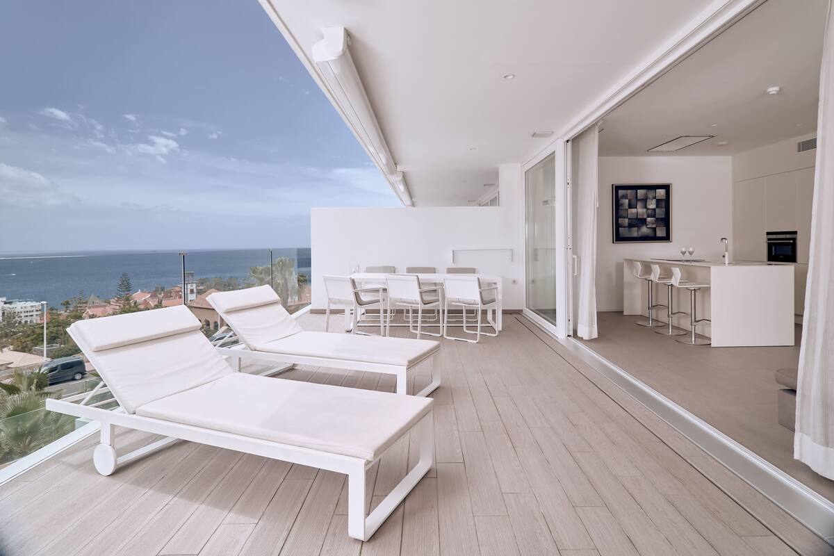 A modern balcony with white lounge chairs and a dining area.