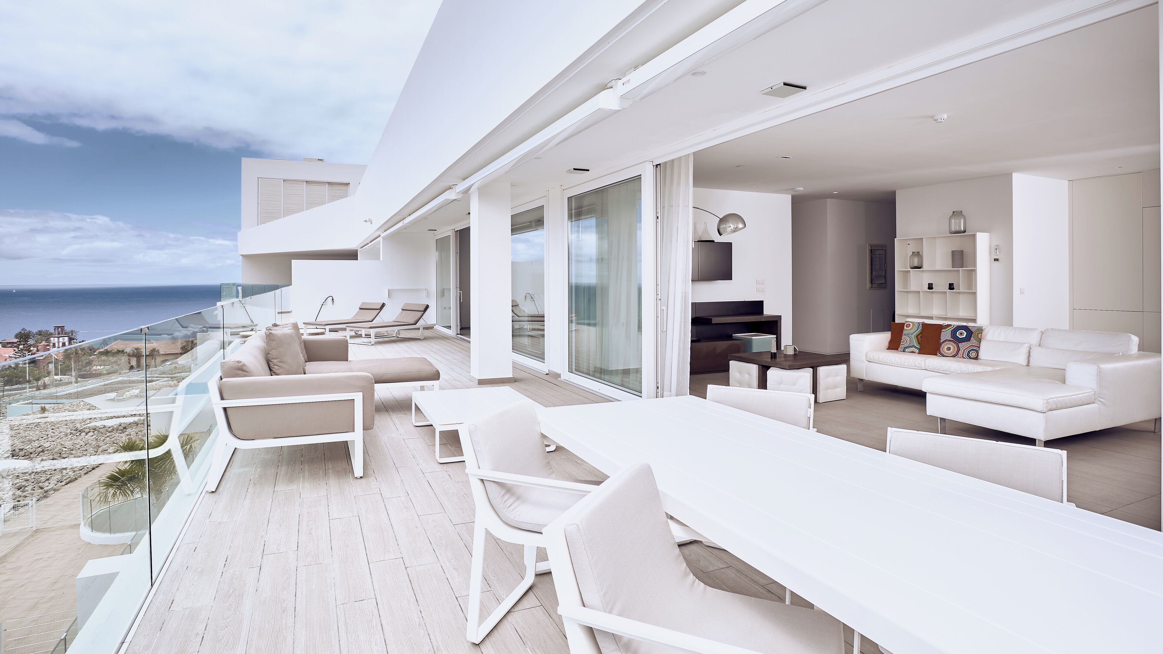 A modern outdoor living area with a white sofa, chairs, and a dining table.