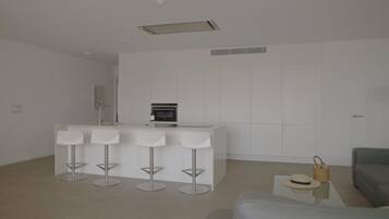A modern kitchen with a central island, four bar stools, a grey sofa, and a small side table with a hat and basket.