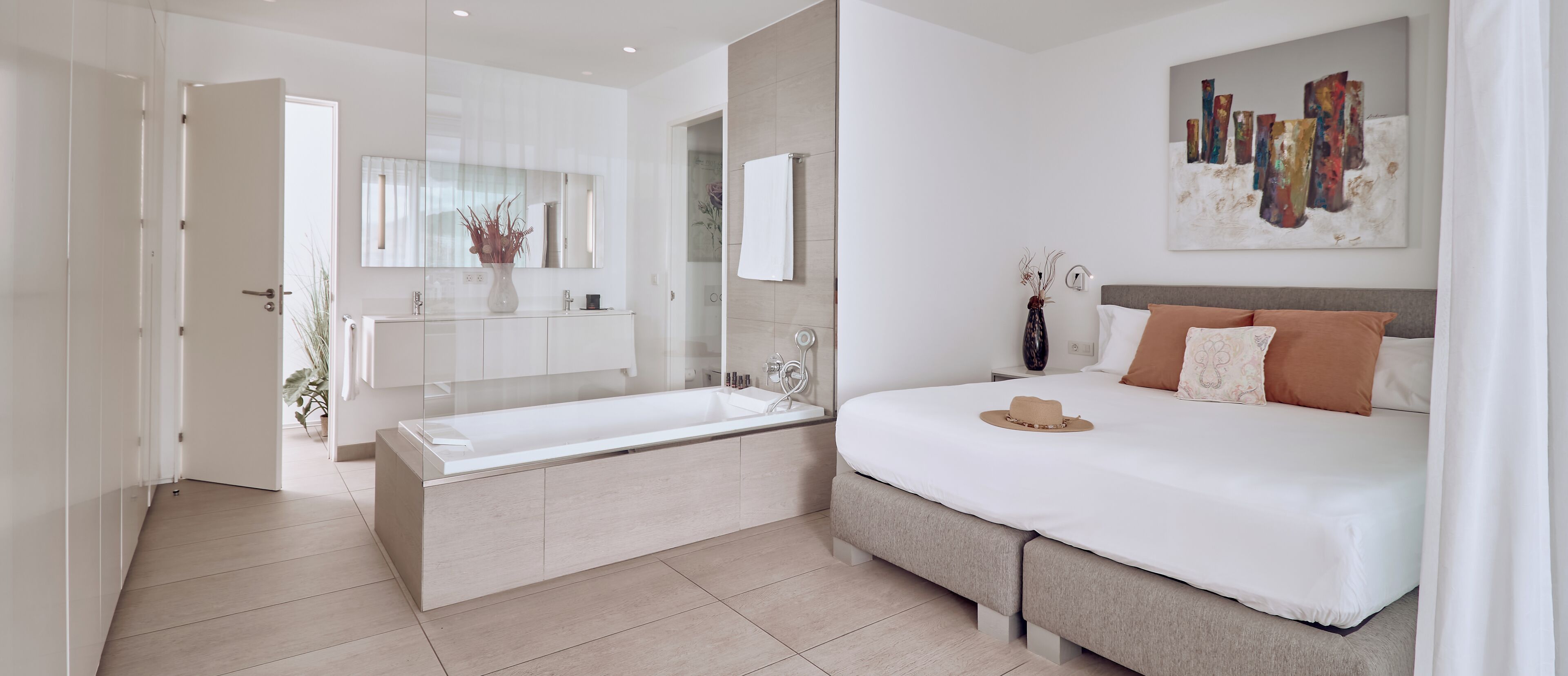 Une chambre moderne avec un grand lit, une table de chevet, une commode, un téléviseur fixé au mur et une salle de bain avec une baignoire et un miroir.