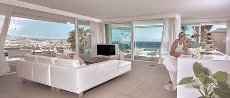 A modern living room with a white sofa, a flat-screen TV, and a dining area with a table and chairs.