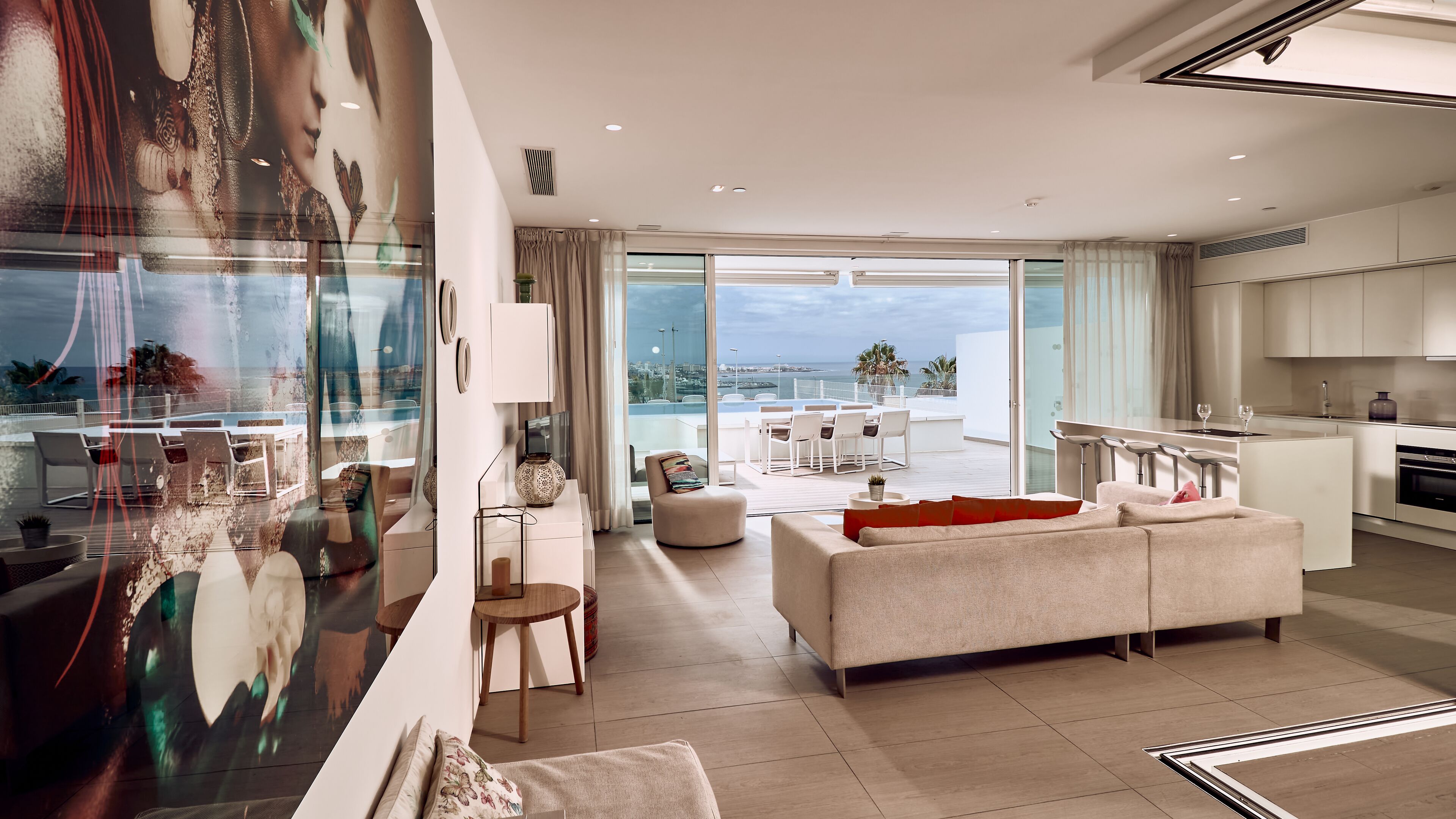 Una sala de estar moderna con sofá, mesa de centro y comedor con sillas. Hay una cocina con estufa y un amplio ventanal con vista al océano.