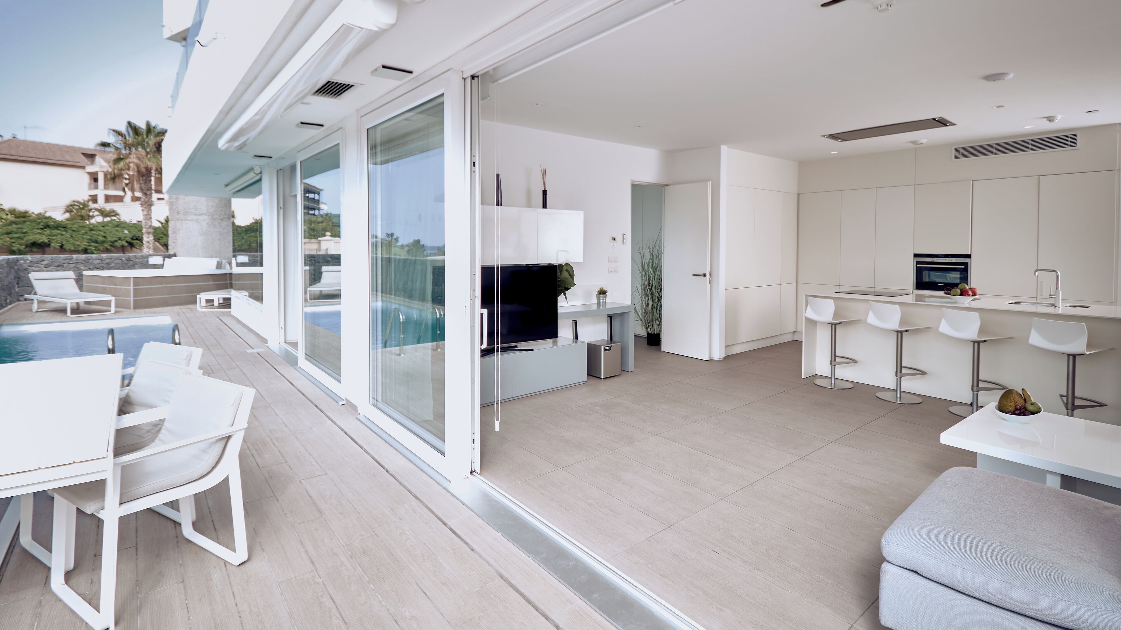 A modern kitchen with a built-in oven, a dining area with white chairs, and a poolside seating area with a table and chairs.