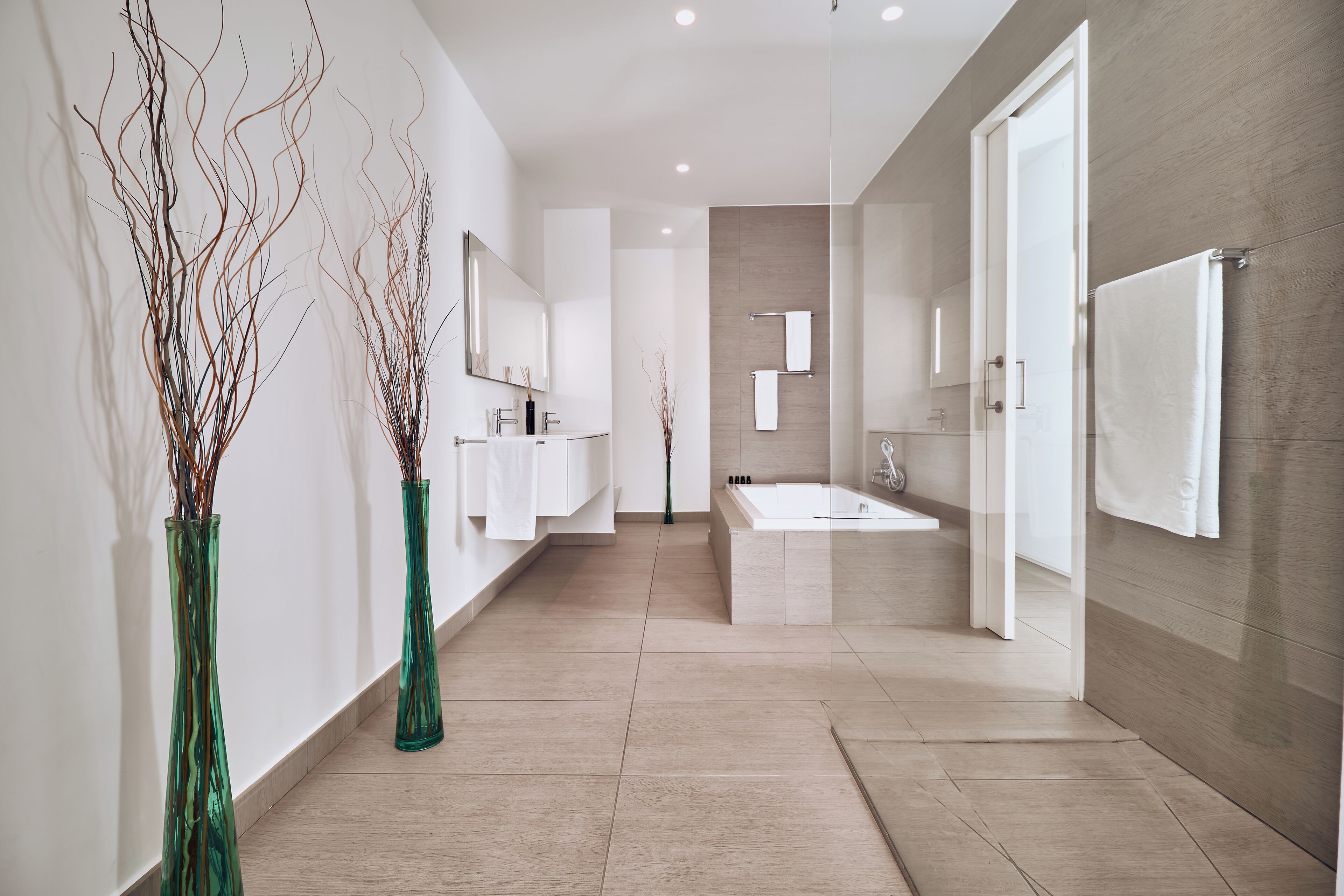 Une salle de bain moderne avec une grande baignoire, un meuble-lavabo et deux vases verts posés sur le sol.