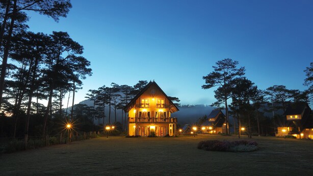 A large, multi-story house with a prominent balcony, surrounded by trees and lit by multiple lights. - Binh An Village Dalat (Xuan Huong - Da Lat)