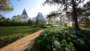 A pathway leading to a building with a pointed roof and a garden with hydrangea flowers. - Binh An Village Dalat (Xuan Huong - Da Lat)
