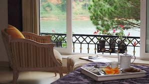 A room with a view of a lake, a wooden chair, a bench, and a breakfast tray with fruits and a teapot. - Binh An Village Dalat (Xuan Huong - Da Lat)