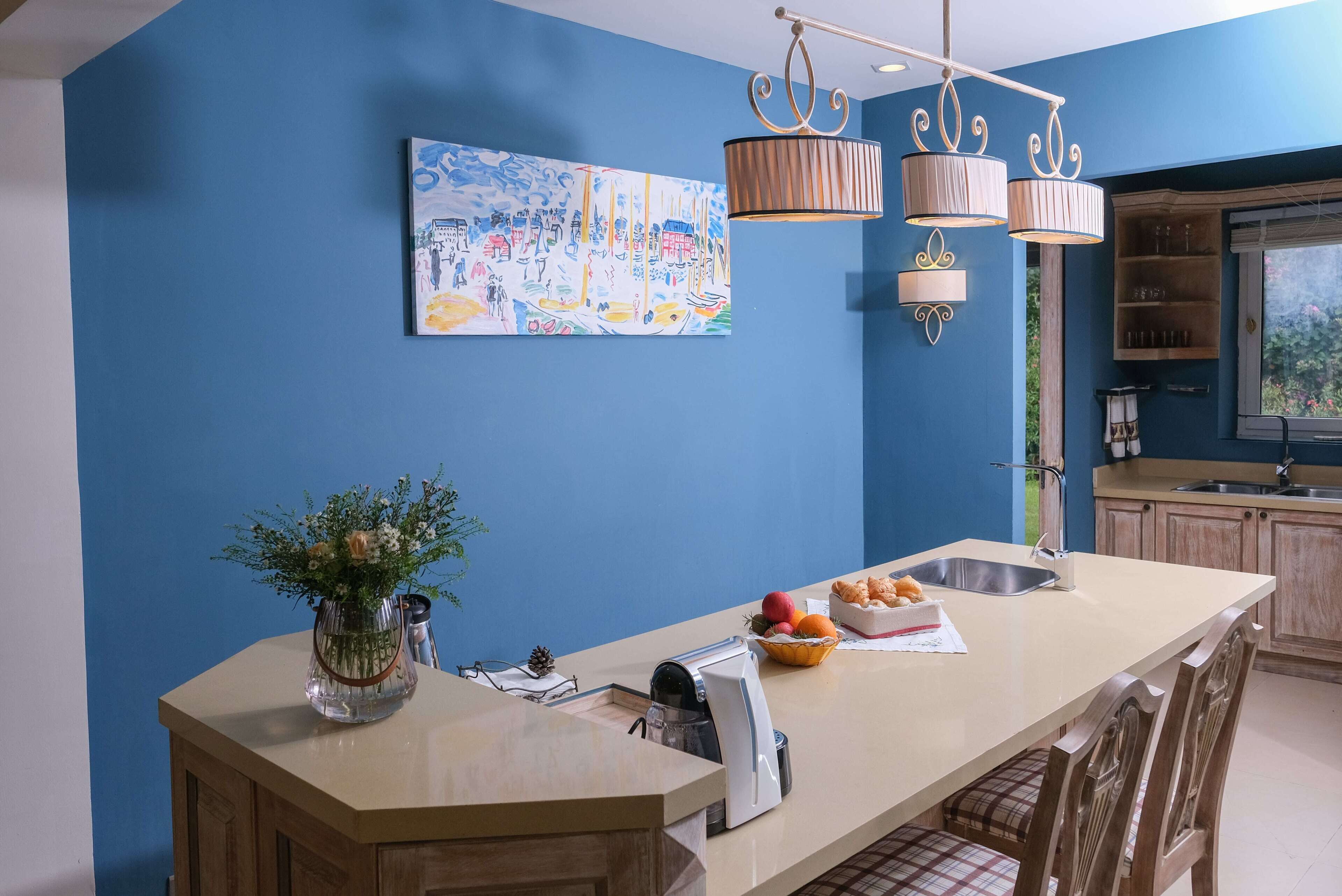 A kitchen with a blue wall, a large island, and a hanging light fixture.