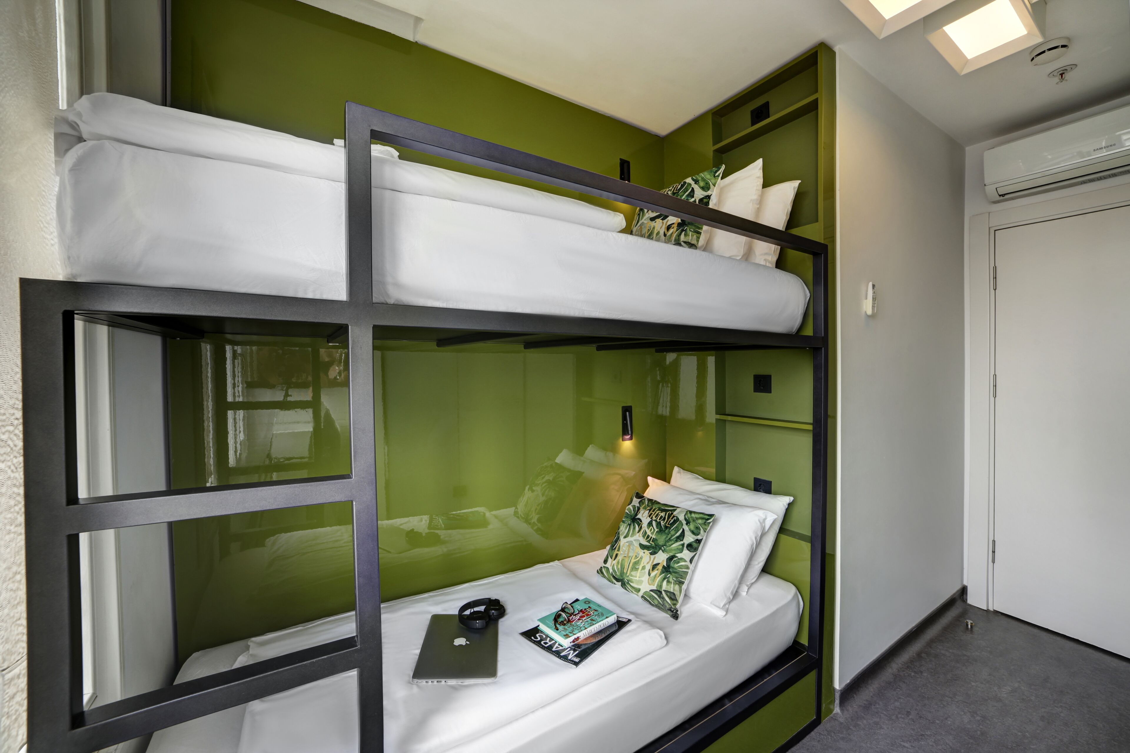 A bunk bed with a laptop and headphones on the lower bunk, a pillow with a leaf pattern, and a book on the bed.