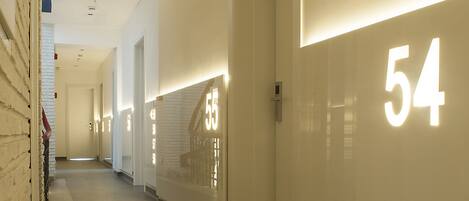 A corridor with illuminated room numbers, a clean floor, and a white brick wall on the left.