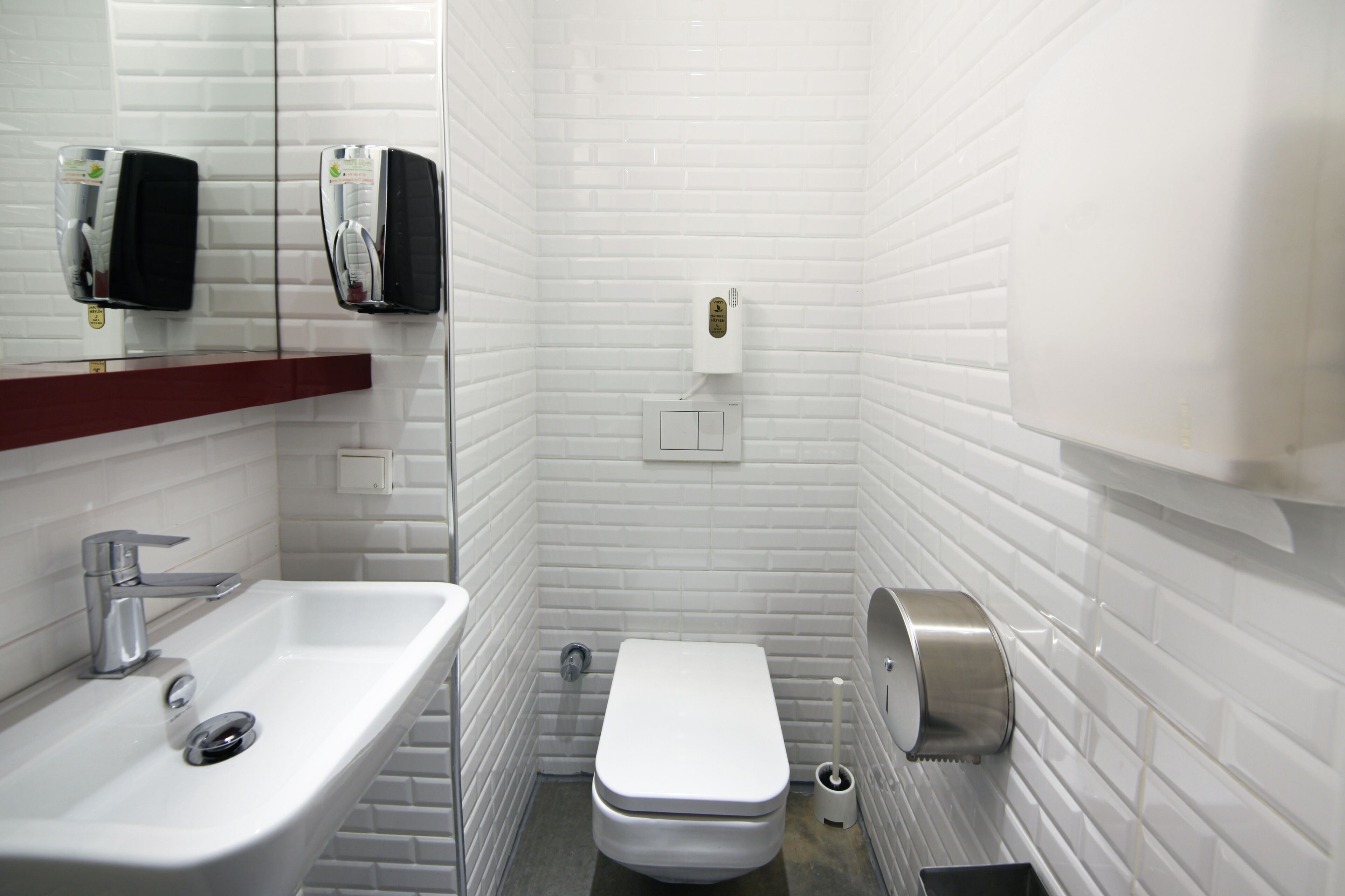 A small, white-tiled bathroom with a sink, toilet, and hand dryer.