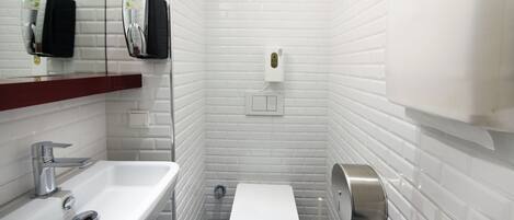 A small, white-tiled bathroom with a sink, toilet, and hand dryer.