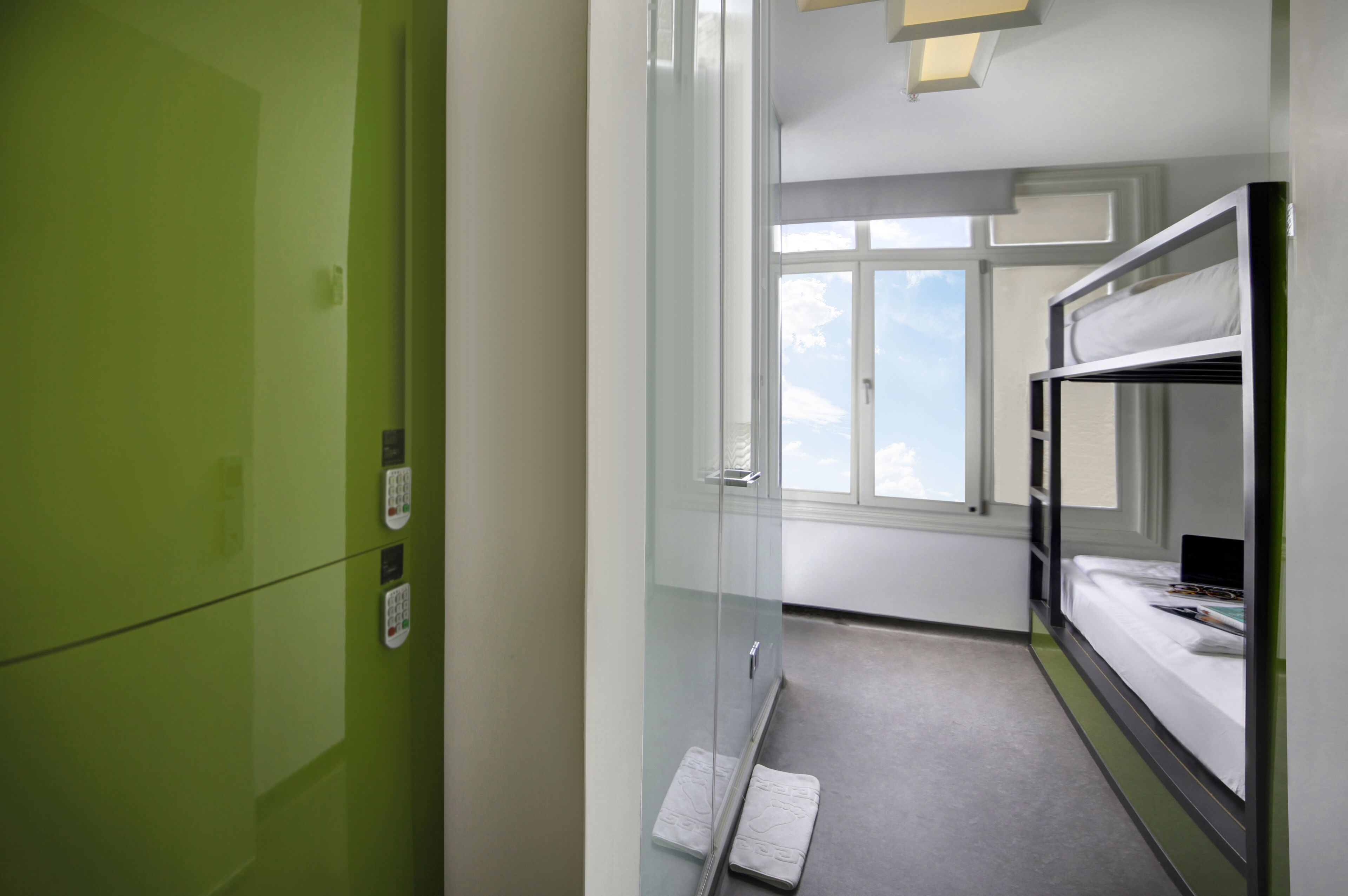 A hotel room with a bunk bed, a glass shower enclosure, and a view of the sky through the window.