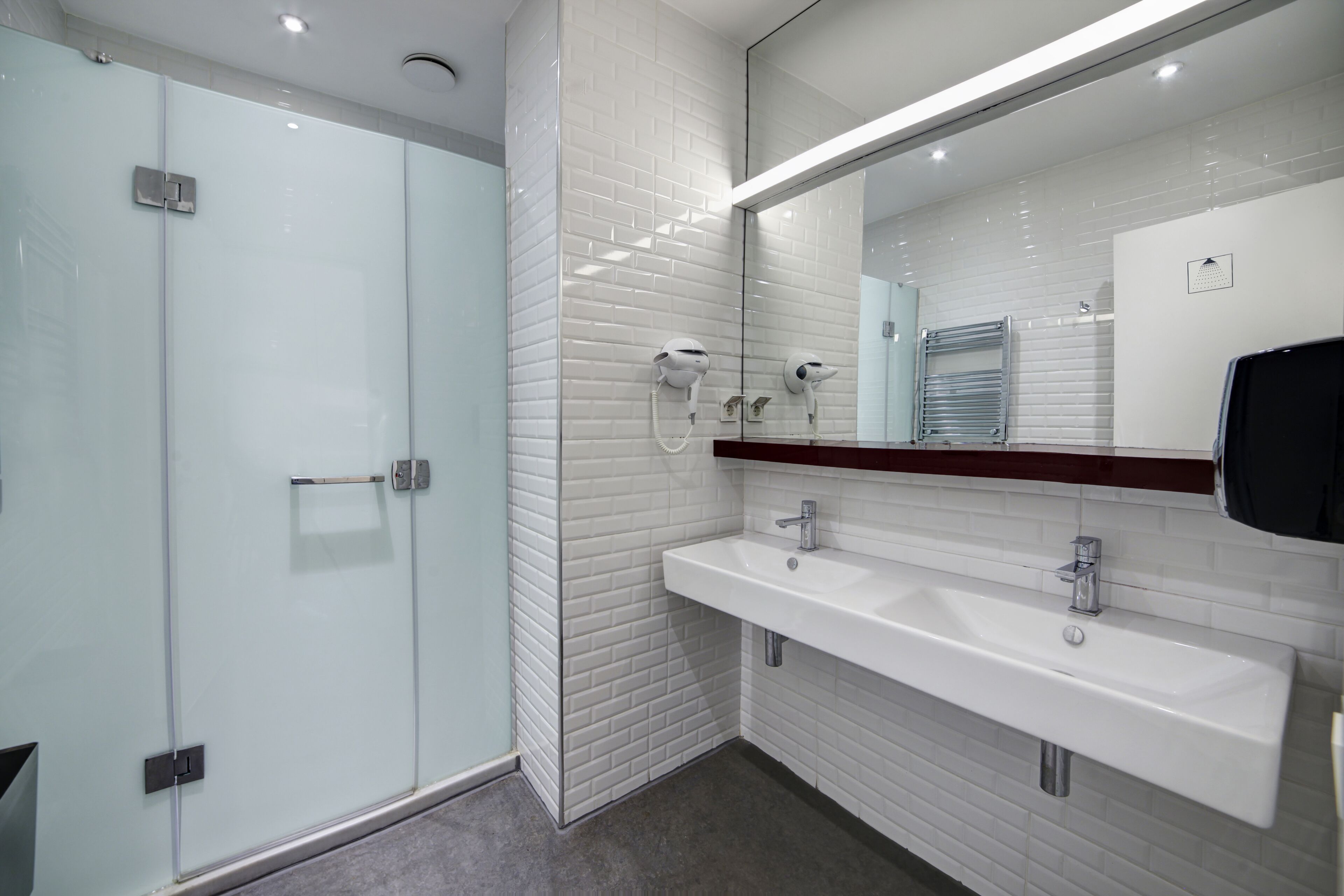 A modern bathroom with a glass shower enclosure, a white sink with a mirror above, and a tiled wall.