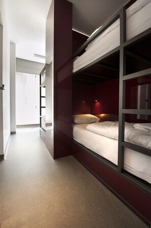 A modern hotel room with bunk beds, a hallway, and a door leading to another room.