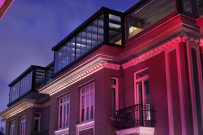 A multi-story building with large windows and balconies, featuring a classic architectural style with detailed moldings and a red facade.