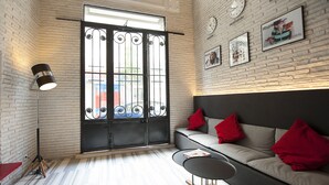 A modern interior with a brick wall, a black-framed window, a grey sofa with red cushions, a small round table, and a floor lamp. - The Central House Istanbul Taksim (Istanbul)