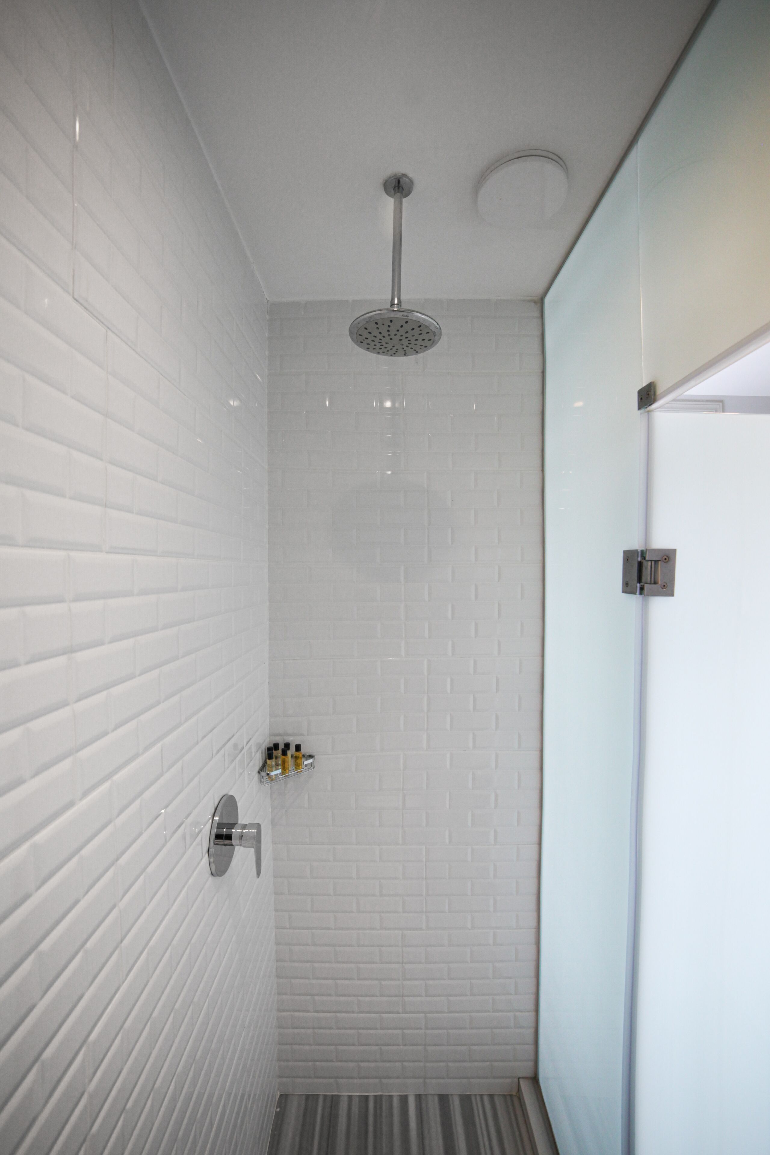 A modern bathroom with white subway tile walls, a shower with a handheld showerhead, and a glass shower door.