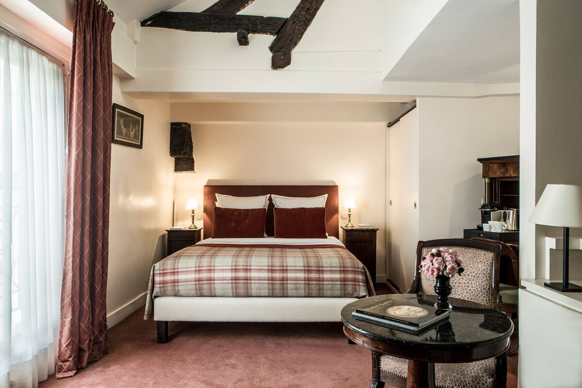 A hotel room with a bed, a table with a vase of flowers, and a chair.