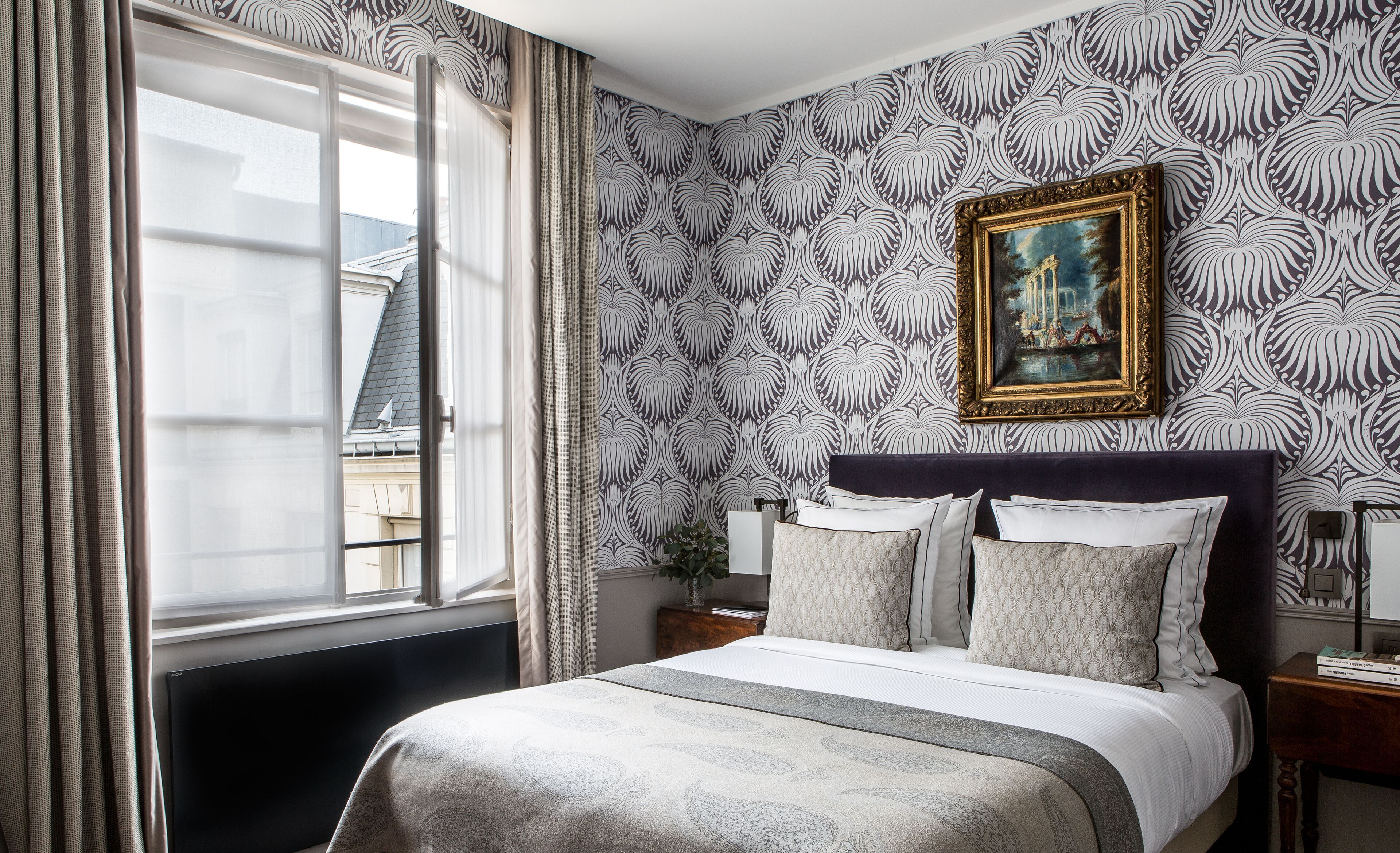 Une chambre d’hôtel avec un lit, des rideaux, un tableau et une vue sur les bâtiments environnants.