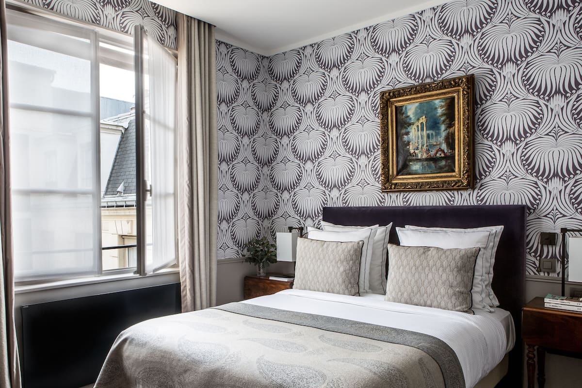 Ein Hotelzimmer mit Bett, Vorhängen, einem Gemälde und Blick auf Gebäude.