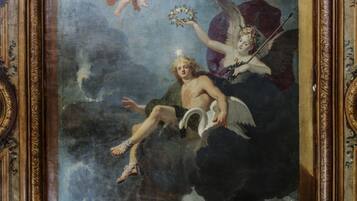 Una pintura clásica con querubines y una figura alada, enmarcada en un borde dorado ornamentado.