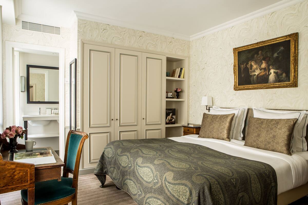 A bedroom with a large bed, a wardrobe, a desk with a chair, and a painting on the wall.