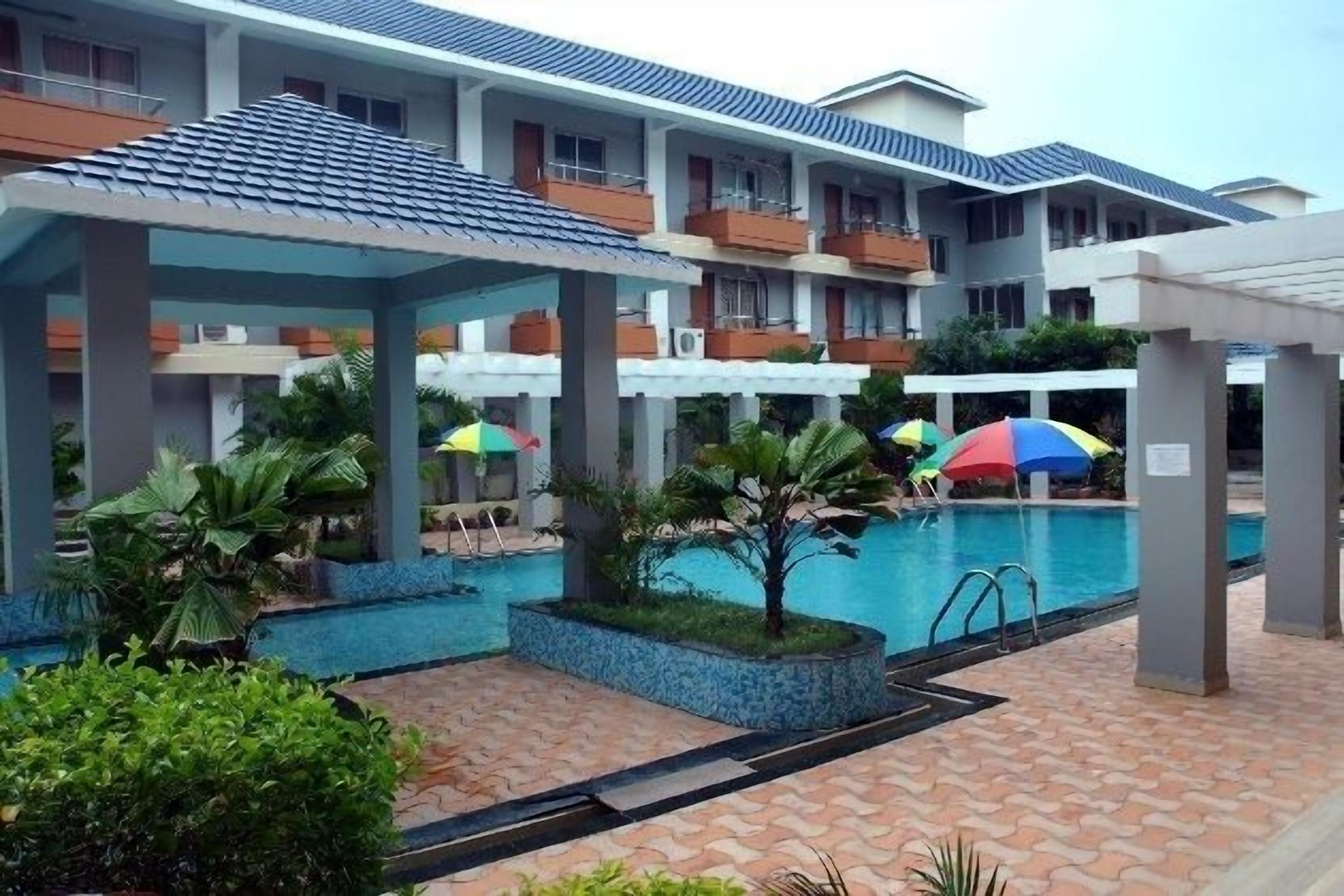 A hotel with a swimming pool, covered outdoor seating areas, and a multi-story building with balconies.