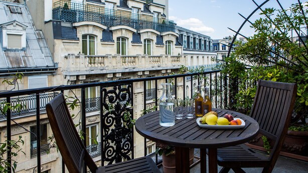 A balcony with a round table, two chairs, a fruit plate, a bottle, and a vase.