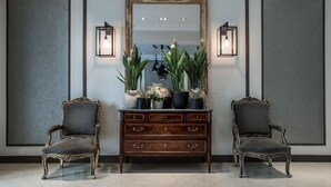 A room with a large mirror, two chairs, a wooden dresser, and wall-mounted lights.