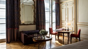 A room with a sofa, a round table with two glasses, a chair, a mirror, and a door with a gold frame.