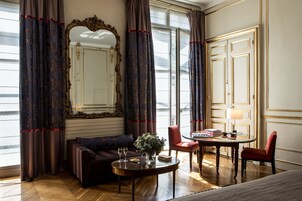 Une pièce comprenant un canapé, une table ronde avec deux verres, une chaise, un miroir et une porte dotée d’un cadre doré.