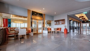 Un hall amplio con diseño moderno, que cuenta con un restaurante llamado "The Coctelero", zonas de estar y una señalización de salida clara.