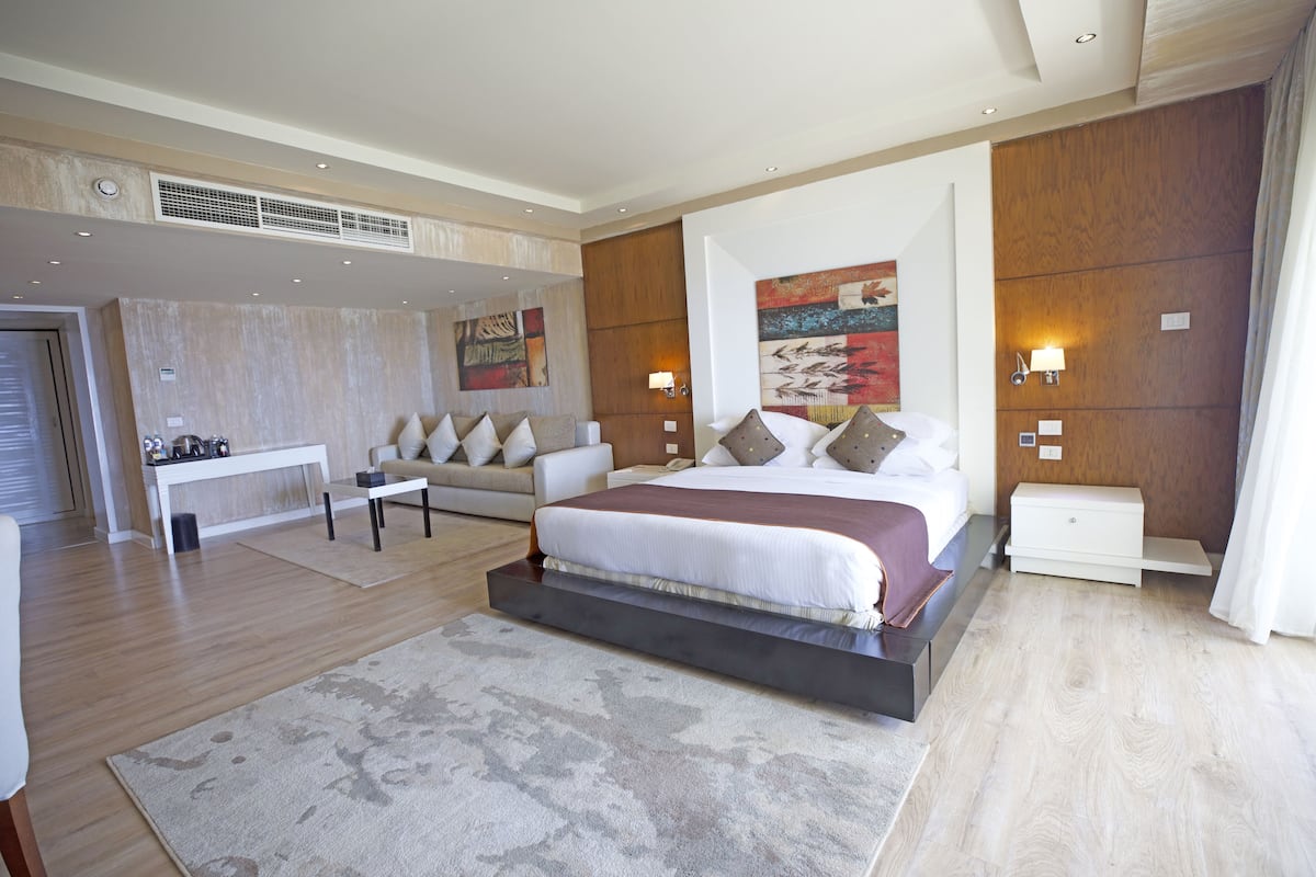 A modern hotel room with a large bed, a sofa, a desk, and a painting on the wall.