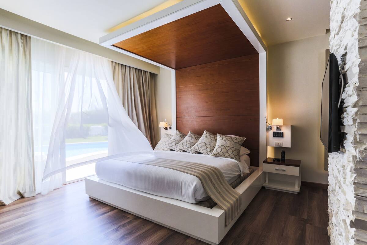 A modern bedroom with a large bed, wooden ceiling, and a stone accent wall.