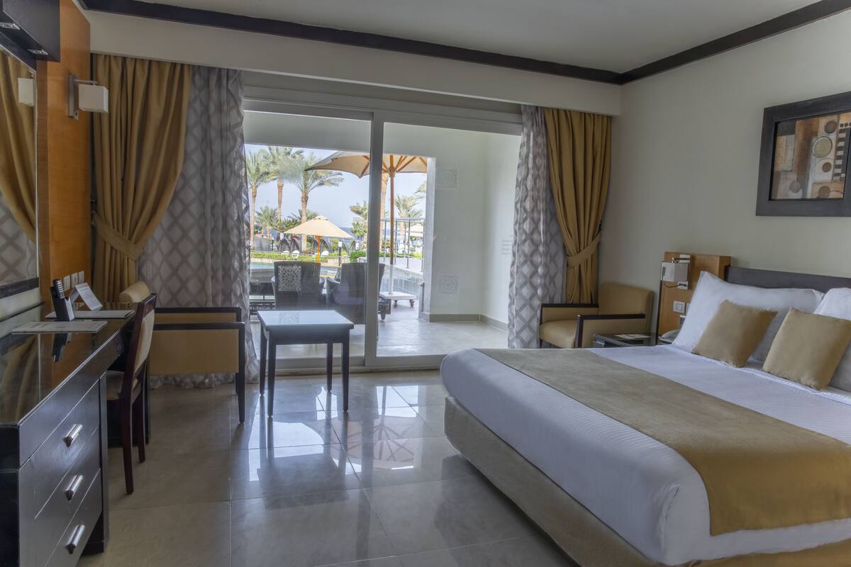 A hotel room with a bed, desk, chair, and a view of the outdoor area.
