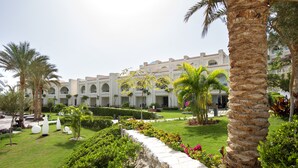 Un hotel con patio que cuenta con palmeras, un muro de piedra y un césped bien cuidado.