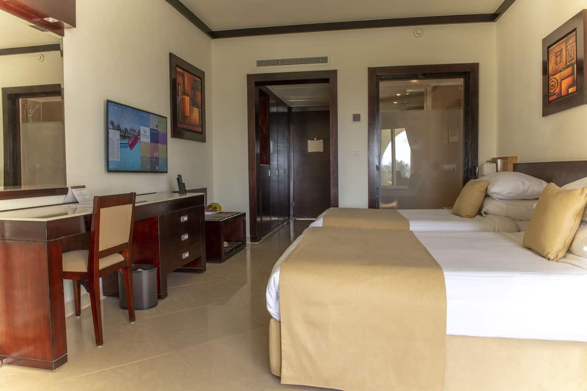 A hotel room with a bed, a desk, a chair, a trash can, and a mirror.