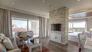 A modern living room with a stone accent wall, a flat-screen TV, and a large sliding glass door leading to a balcony. - SUNRISE Montemare Resort Grand Select (Sharm El Sheikh)