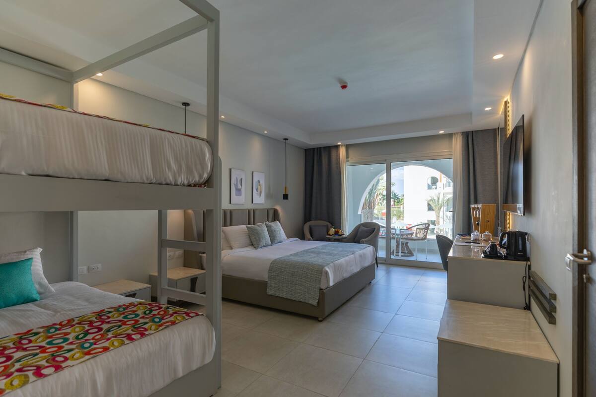 A hotel room with a bunk bed, a desk with a chair, a small table, and a view of the outside.