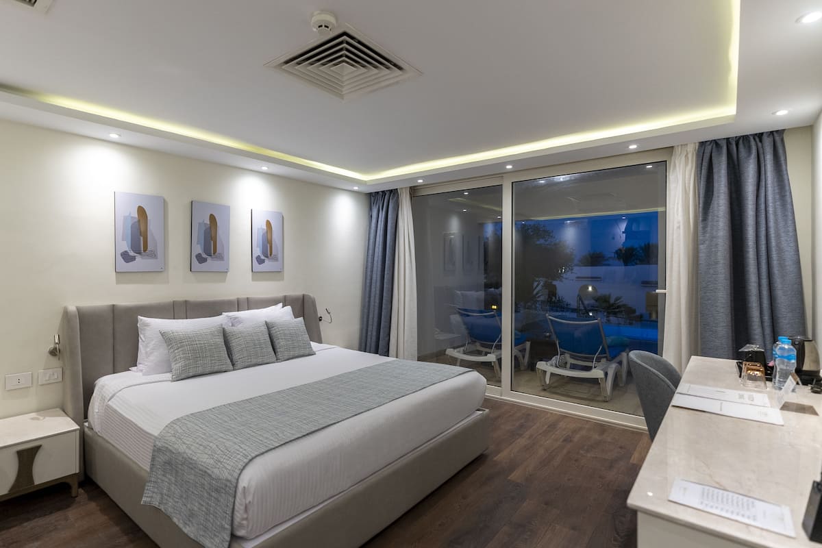 A modern hotel room with a large bed, a desk, and a view of a pool.
