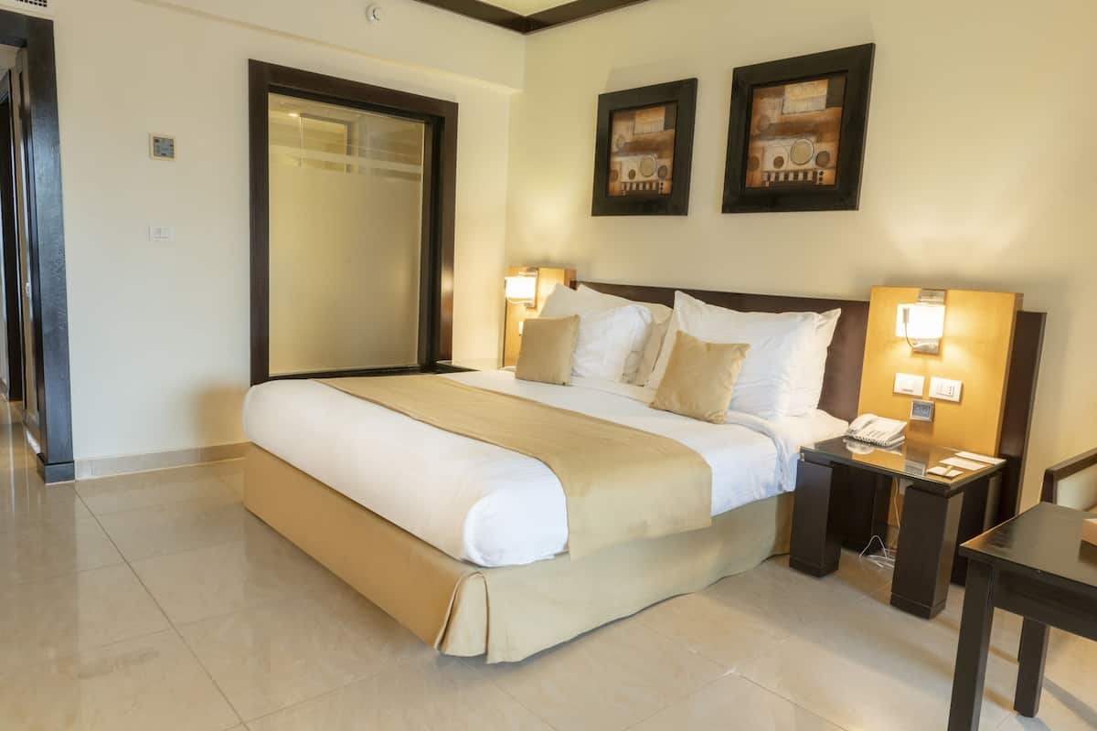 A hotel room with a large bed, bedside lamps, a bedside table, and a small desk.