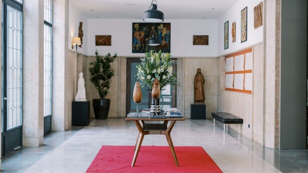 A spacious lobby with a red carpet, a modern table with decorative items, a hanging light fixture, and artwork on the walls.